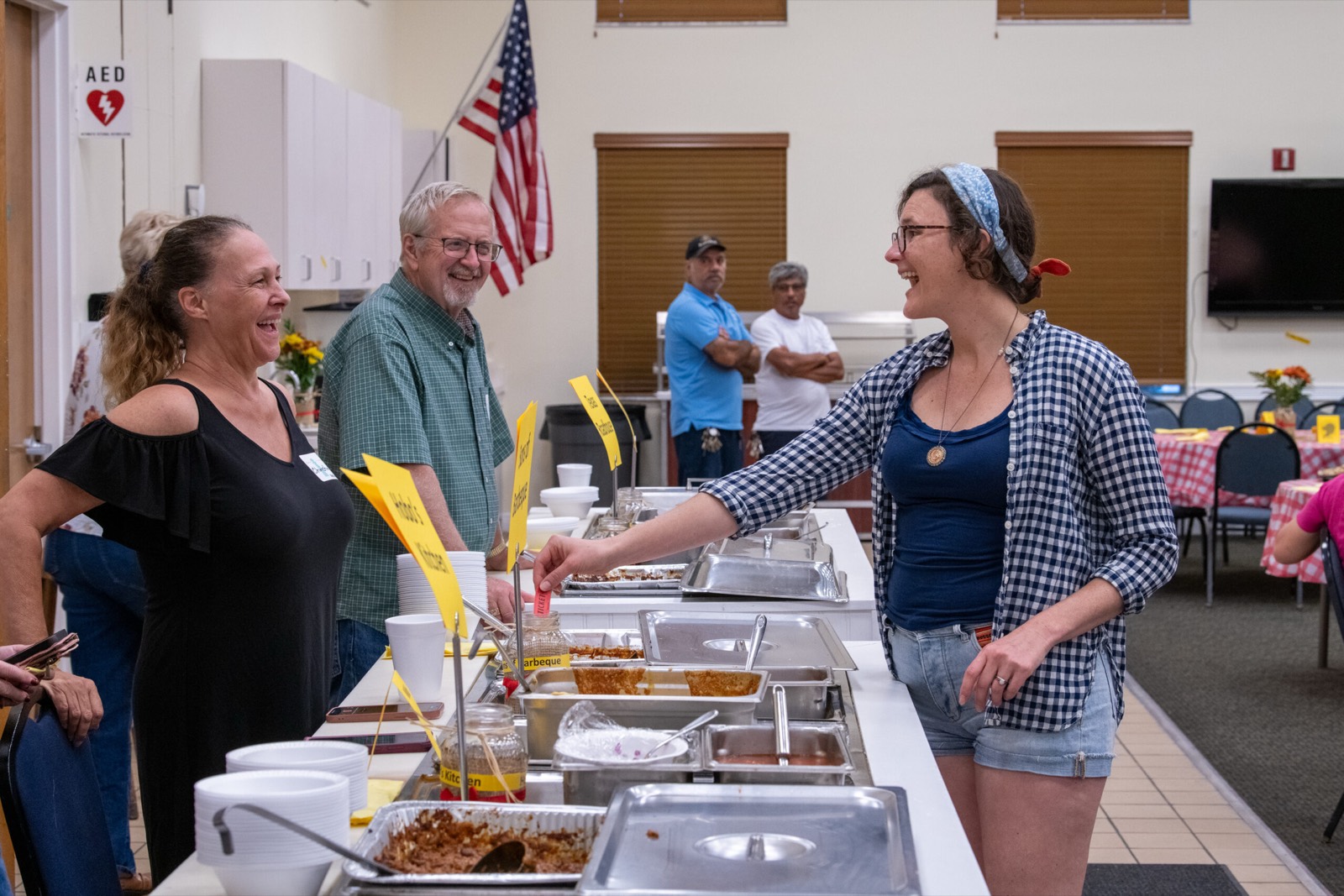 Volunteers laughing together while serving chili from warming trays at the chili cook-off
