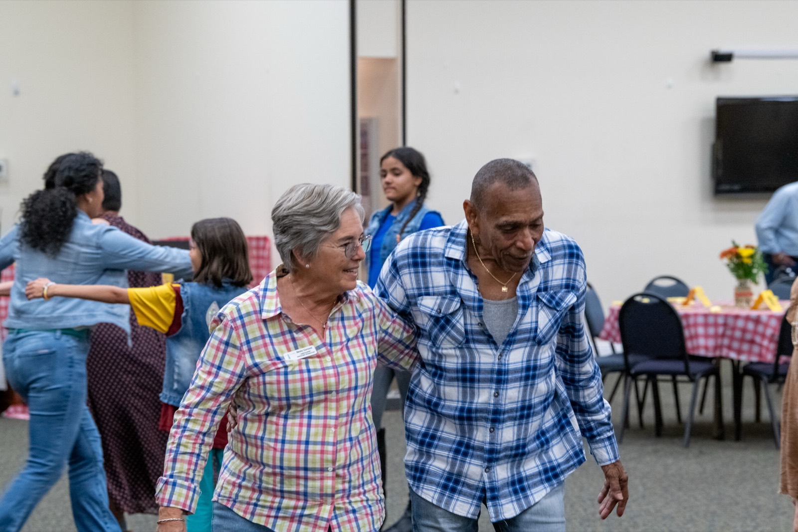 Two people arm in arm and smiling as they line dance together at a LightHouse PBC community fundraiser