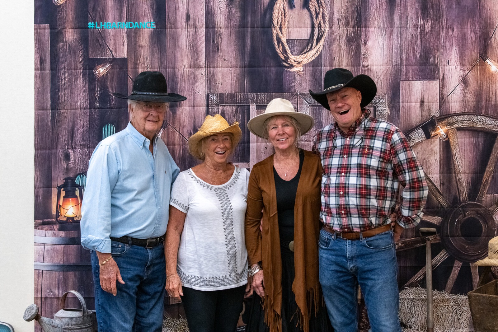 Four guests in cowboy hats posing together in front of the barn photo backdrop
