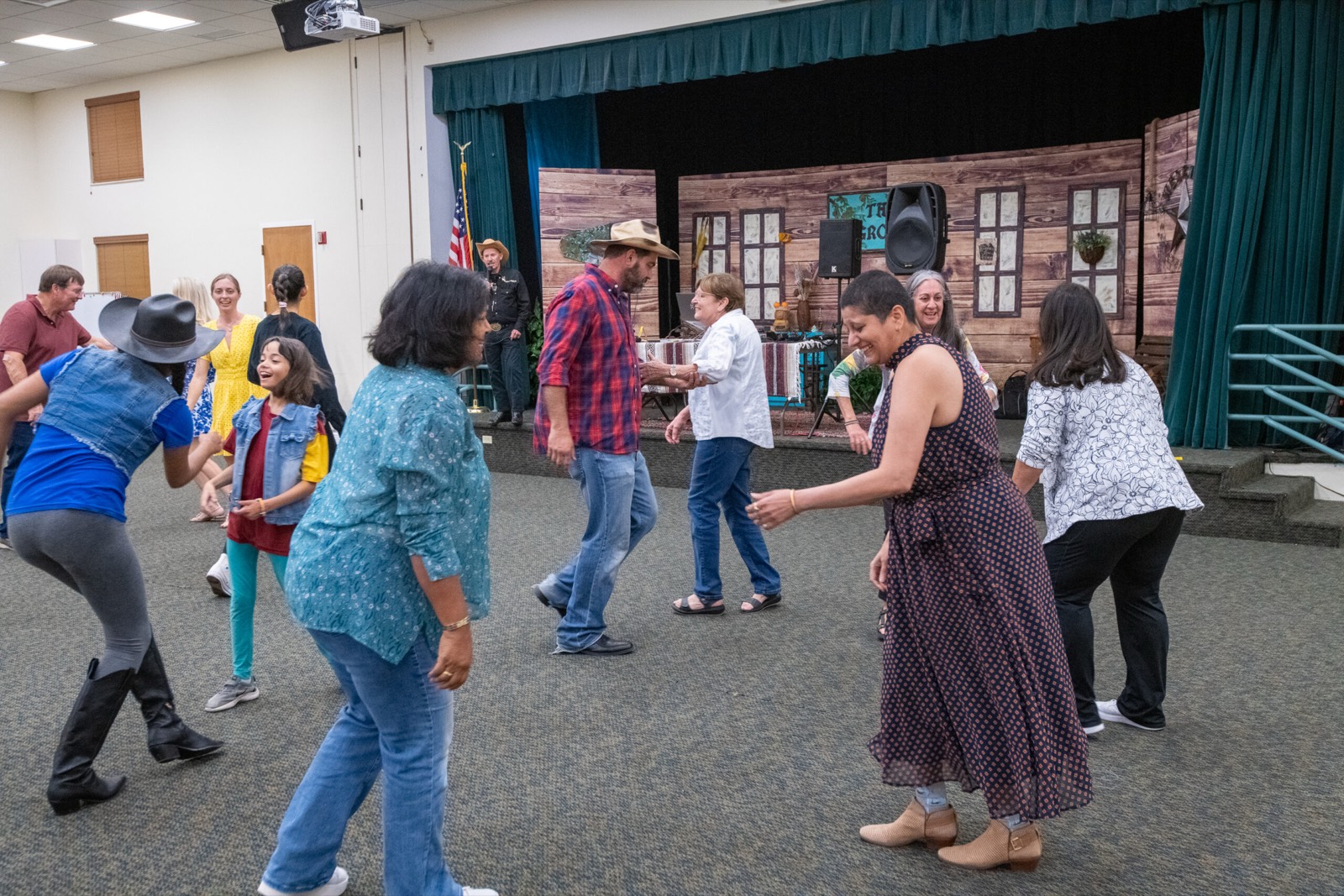 A room full of guests line dancing in front of a barn backdrop at the 2025 LightHouse PBC Barn Dance