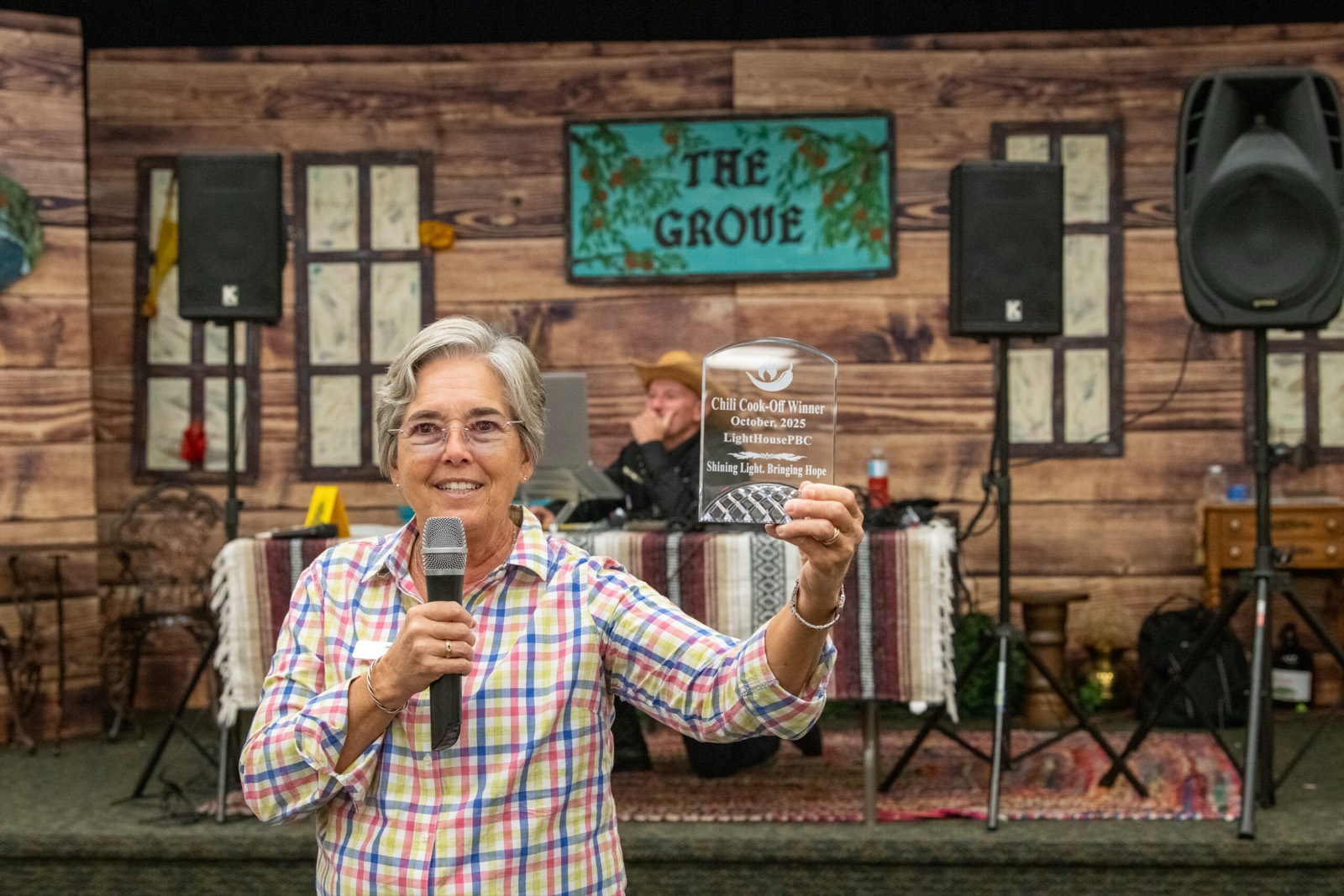 Becky Dymond holding a microphone and raising an award on stage at the Barn Dance