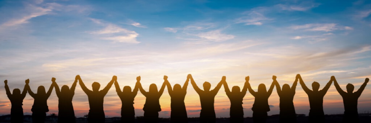 A line of people standing shoulder to shoulder with their hands raised and joined against a sunset sky